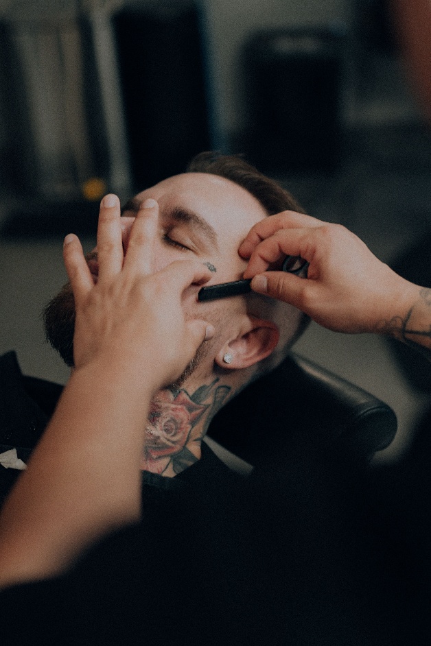 A barber carefully styling a young man’s beard at a barber shop.